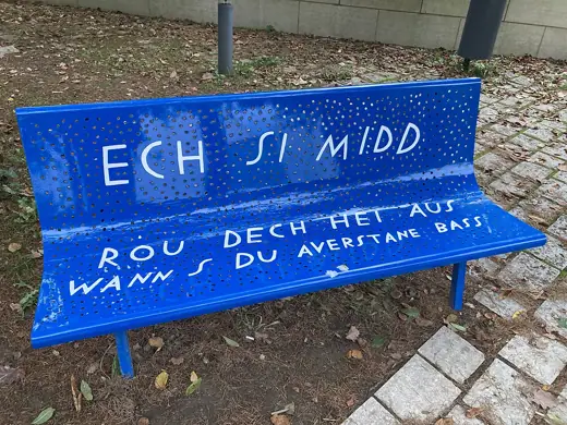 Photo 4: Exterior · Banc bleu à côté du MUDAM, avec l'inscription "Ech si midd - rou dech hei aus wann s du averstane bass