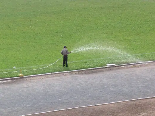 Photo 5: Context · Homme arrosant la pelouse du stade olympique de Phnom Penh, Cambodge