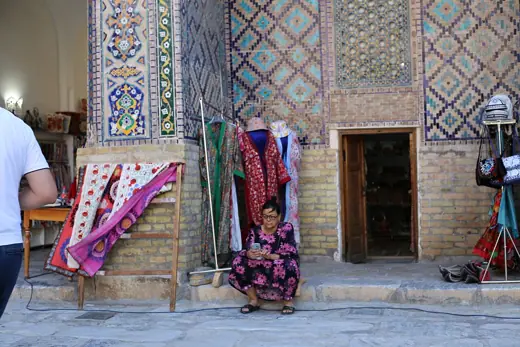 Photo 2: Exterior · A local woman sits beside a richly tiled wall in the Registan ensemble