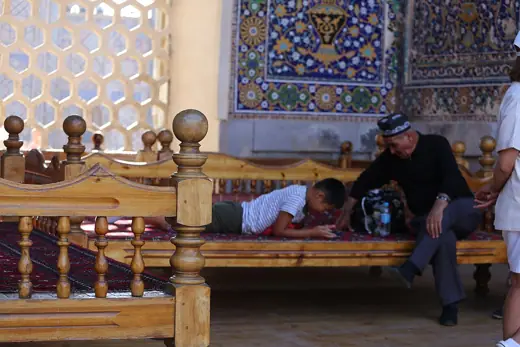 Photo 4: Interior · People rest on a traditional raised platform inside a richly tiled historic courtyard at Registan