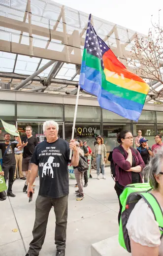 Photo 4: Exterior · A protester holds a rainbow American flag at a DACA rally in San Francisco